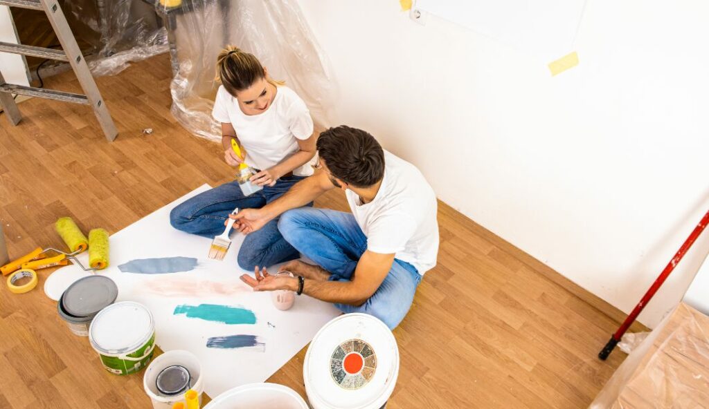 A couple sits on the floor going over different paint color samples
