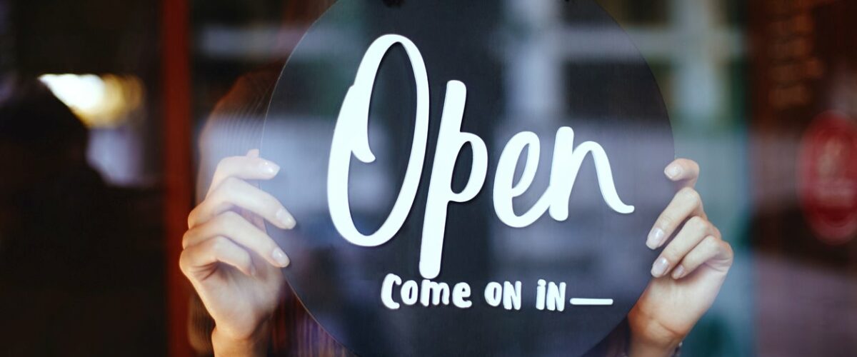 A woman adjusting a sign that reads “Open come on in”