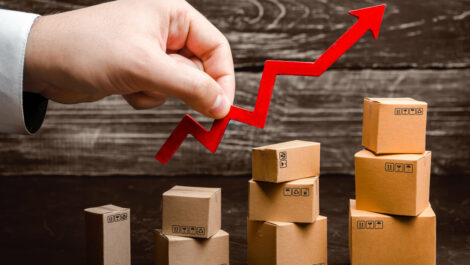 A hand holding a rising arrow above growing stacks of boxes.