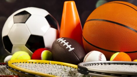 A close-up composition of various sports balls and pieces of sports equipment resting together on grass.